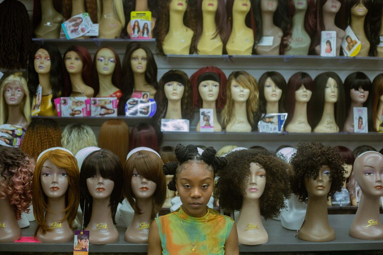 Black woman in the hair shop with Bantu Knots next to wig heads with wigs